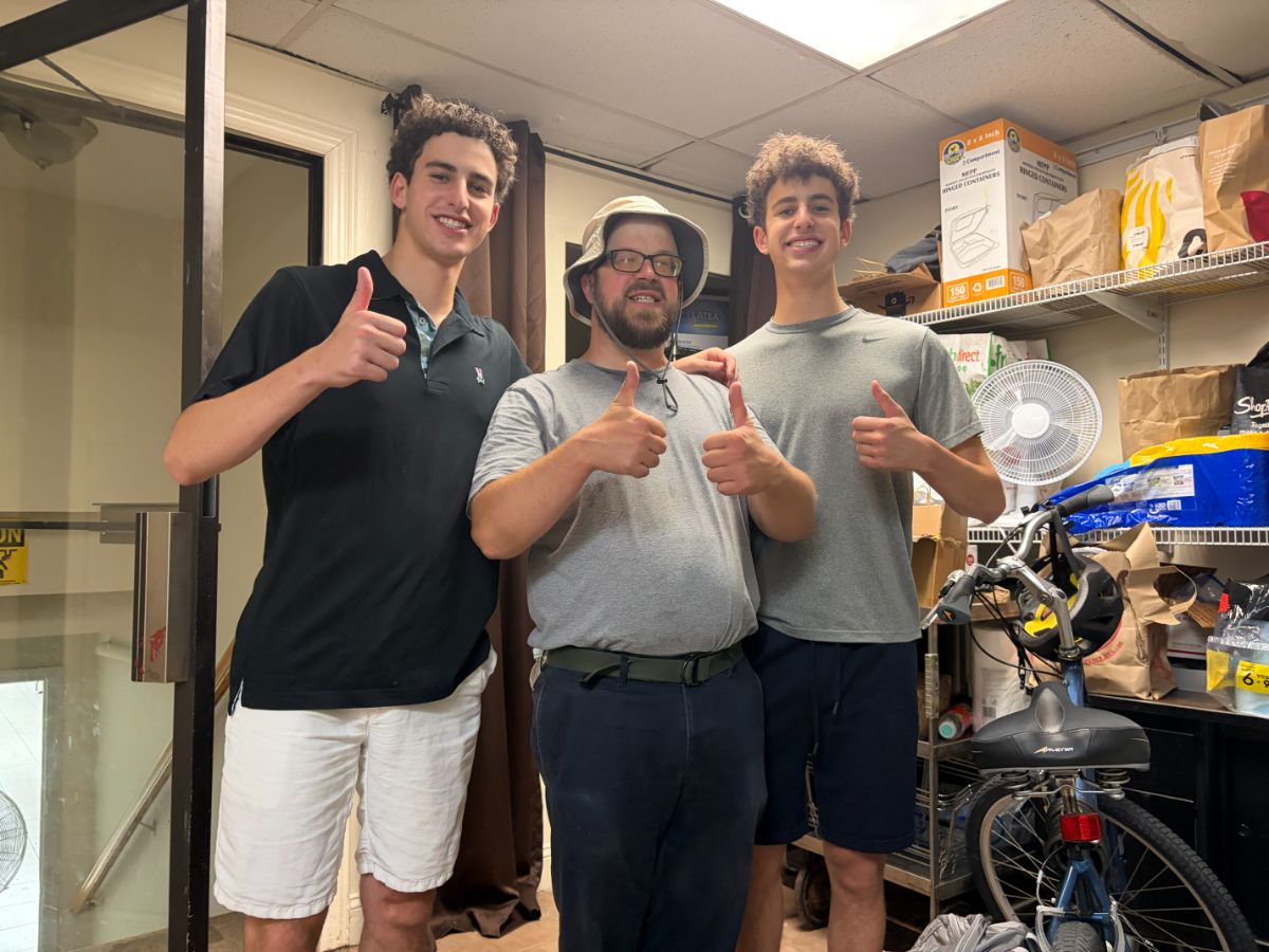 Daniel and Liam Wellisch with a CSA Kitchen volunteer, giving a thumbs up in the kitchen storeroom