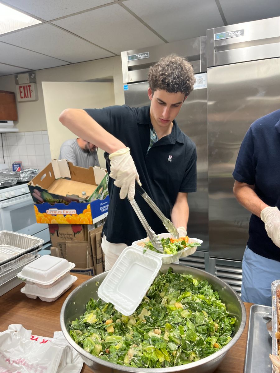 A volunteer tossing a large bowl of fresh salad in the kitchen